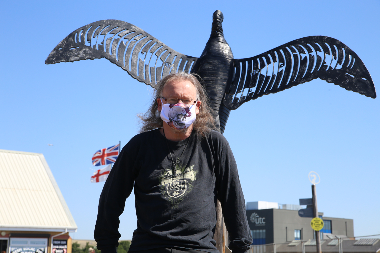 Mask wearing man in front of bird sculpture